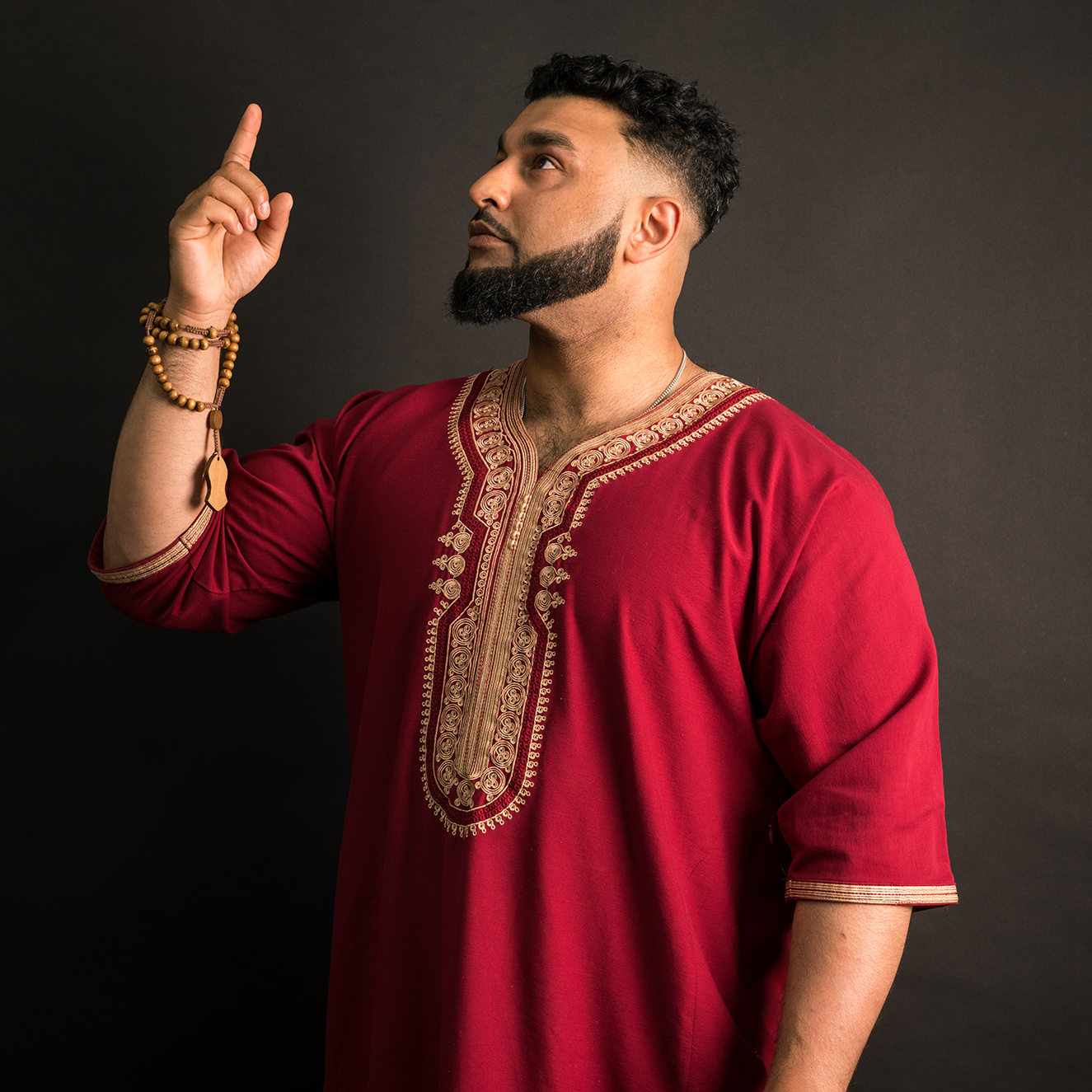 Asim The Poet in red pointing at the sky with black background